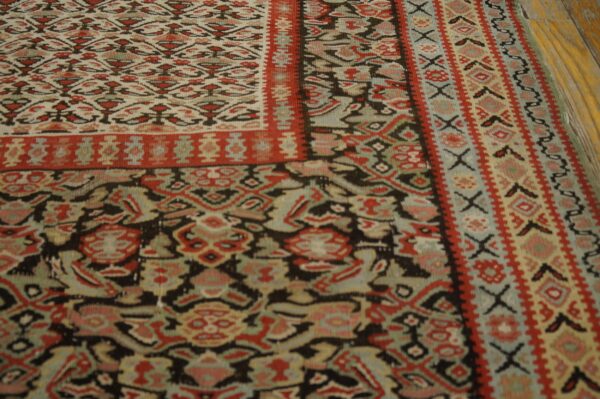 Geometric rug in faded red, black, and cream with teal accents lying on distressed wood flooring.