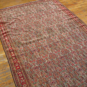 A large, faded red and beige rug with repeating paisley motifs rests on a glossy wood floor.