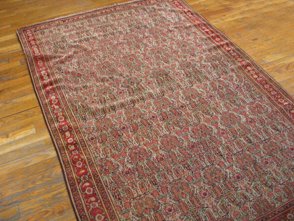 A large, faded red and beige rug with repeating paisley motifs rests on a glossy wood floor.