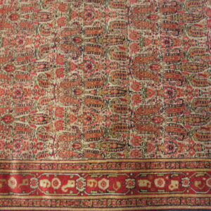 Rug detail showing a dense red and cream paisley field meeting a multi-layered red floral border.