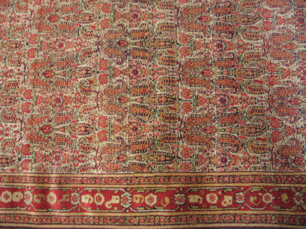 Rug detail showing a dense red and cream paisley field meeting a multi-layered red floral border.