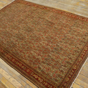 Traditional red and beige rug with intricate repeating pattern laid on light, worn hardwood floorboards.