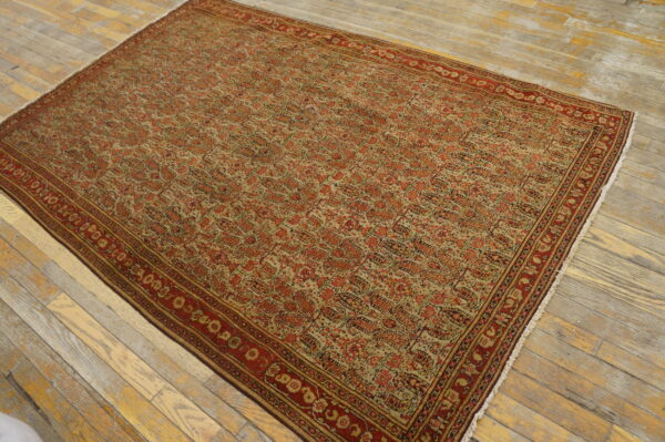 Traditional red and beige rug with intricate repeating pattern laid on light, worn hardwood floorboards.