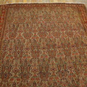 Traditional red and tan rug with dense boteh design and floral border rests on worn wooden flooring.