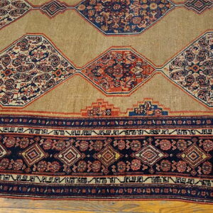 Tan rug featuring large navy and red ornate diamond medallions and a geometric border on wood floor.