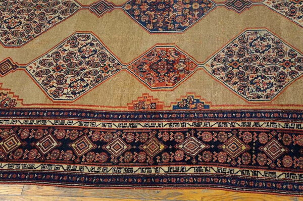 Tan rug featuring large navy and red ornate diamond medallions and a geometric border on wood floor.