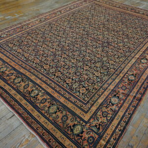 An intricate floral rug featuring navy, coral, and beige borders rests on distressed wood plank flooring.