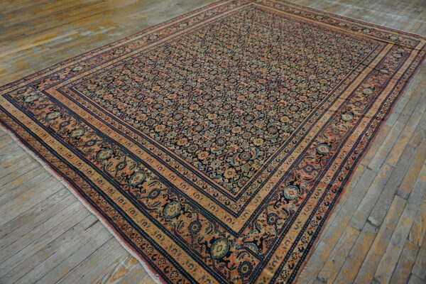 An intricate floral rug featuring navy, coral, and beige borders rests on distressed wood plank flooring.