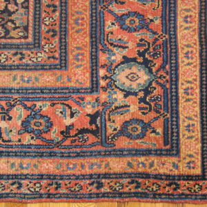 Ornate traditional rug corner displaying floral designs in terracotta, navy, and gold on a wood floor.