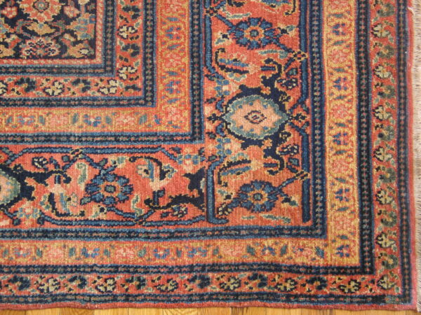 Ornate traditional rug corner displaying floral designs in terracotta, navy, and gold on a wood floor.