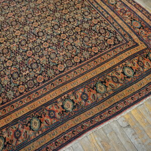 Low-pile rug with a dense navy, coral, and gold floral pattern lays on rustic grey wood flooring.