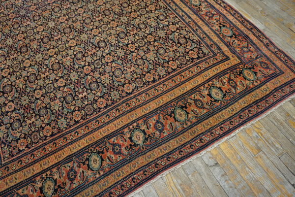 Low-pile rug with a dense navy, coral, and gold floral pattern lays on rustic grey wood flooring.