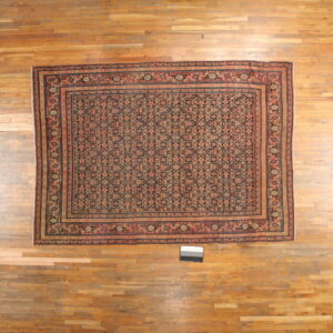 Densely patterned rug featuring coral, teal, and dark blue motifs displayed on light, worn wood flooring.