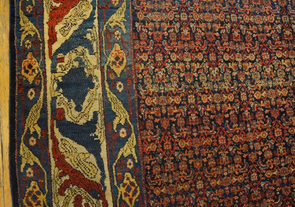 Blue, red, and gold patterned rug displaying a dense field and ornate border on wood flooring.