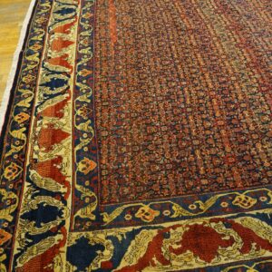 Red and blue patterned rug with wide ornamental borders covering a wood floor.
