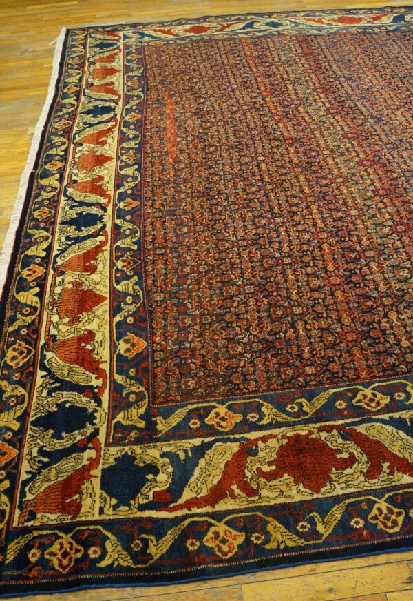 Red and blue patterned rug with wide ornamental borders covering a wood floor.
