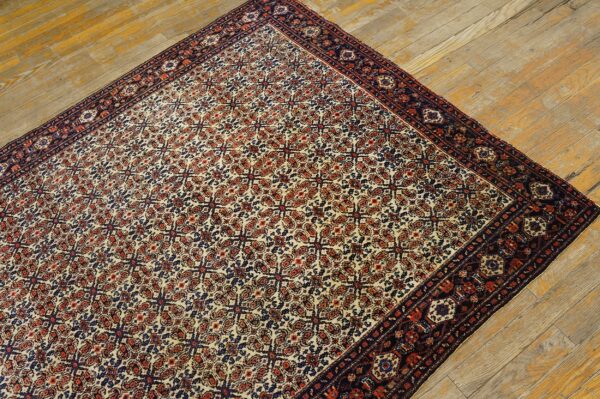 Cream, rust, and blue patterned rug with a wide dark border rests on rustic wood planks.