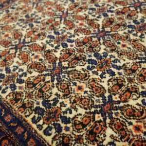 Detailed traditional rug pattern in cream, navy blue, and rust orange with a plush texture.