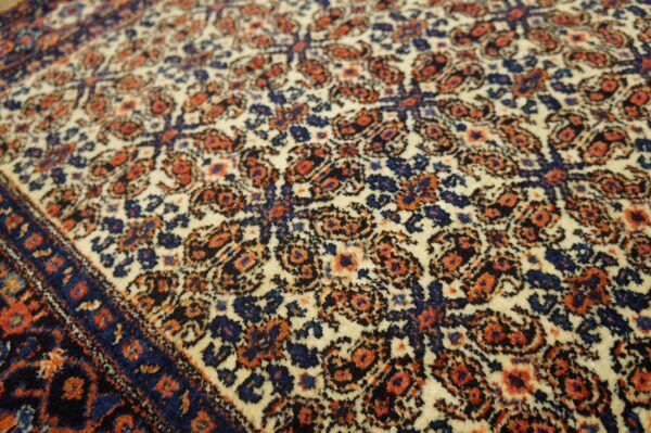 Detailed traditional rug pattern in cream, navy blue, and rust orange with a plush texture.