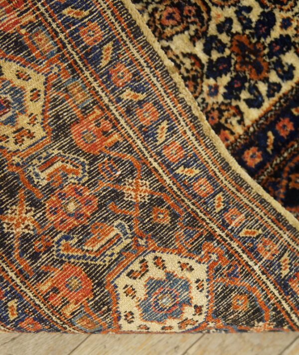 Detailed view of a navy, orange, and cream patterned rug border folded on wood flooring.