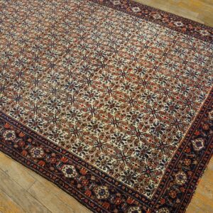 Low-pile rug with a detailed cream, rust, and navy trellis pattern on yellow-toned plank flooring.