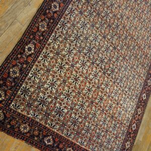 Cream and rust traditional rug with a dark border and dense pattern lies on distressed wood floorboards.