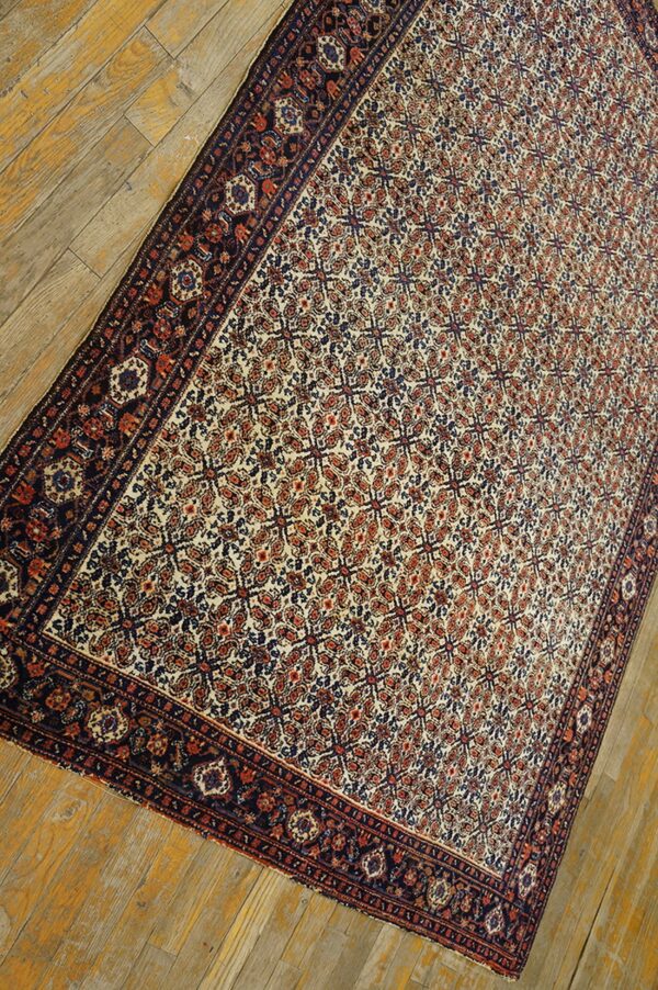 Cream and rust traditional rug with a dark border and dense pattern lies on distressed wood floorboards.