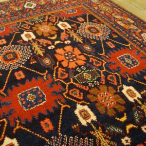 Traditional high-pile rug with geometric and stylized floral motifs in navy, red, and cream on wood.