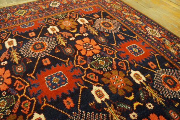 Traditional high-pile rug with geometric and stylized floral motifs in navy, red, and cream on wood.