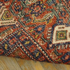 Close-up of a densely woven rug with red, blue, and cream geometric motifs on wood floor.