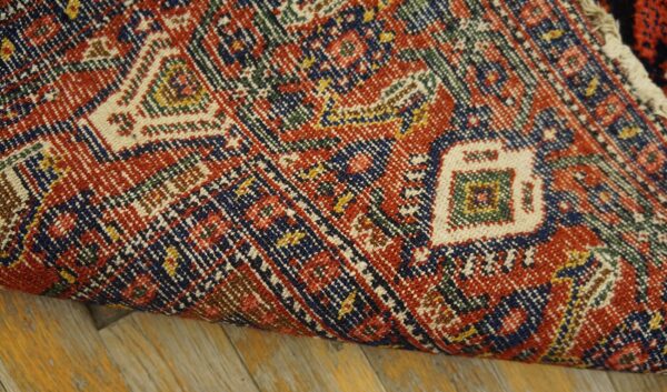Close-up of a densely woven rug with red, blue, and cream geometric motifs on wood floor.