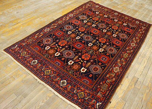 Navy and rust colored traditional rug with stylized motifs placed on pale, plank wood flooring.