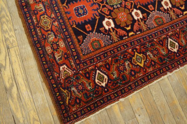 A traditional red and navy rug with geometric patterns rests on light, distressed hardwood flooring.