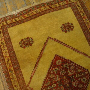 Golden yellow rug featuring a stepped red prayer design and ornate borders on distressed wooden flooring.