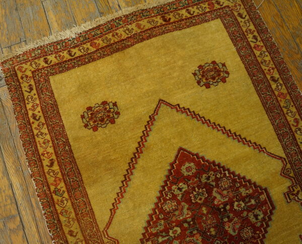 Golden yellow rug featuring a stepped red prayer design and ornate borders on distressed wooden flooring.
