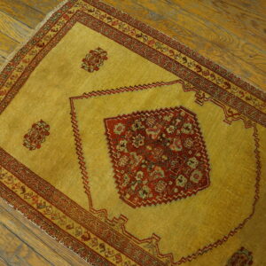Golden yellow low-pile rug with detailed red medallion and borders rests on a textured wood floor.