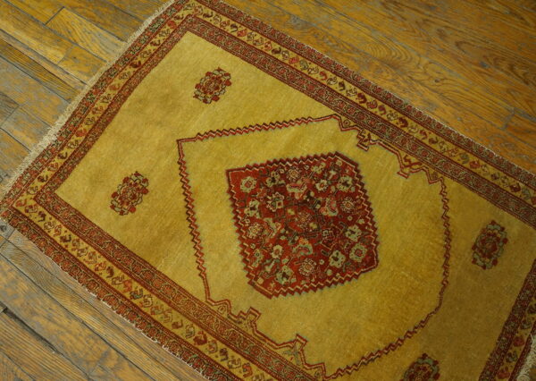 Golden yellow low-pile rug with detailed red medallion and borders rests on a textured wood floor.