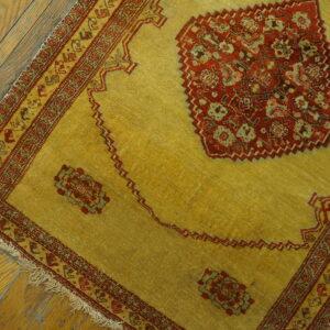 Golden-yellow rug with deep red and green geometric patterns sits on worn wooden plank flooring.