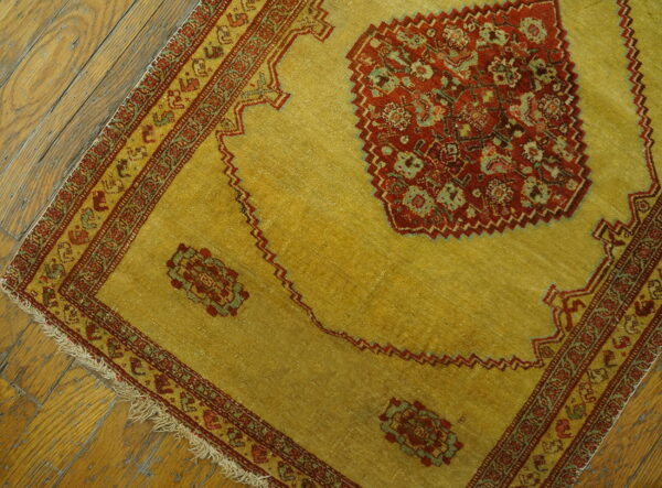 Golden-yellow rug with deep red and green geometric patterns sits on worn wooden plank flooring.