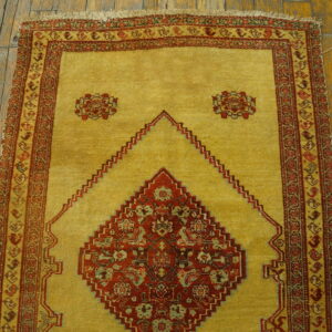 Golden yellow rug featuring a red stepped diamond pattern and detailed multi-banded border on wood floors.