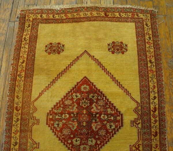 Golden yellow rug featuring a red stepped diamond pattern and detailed multi-banded border on wood floors.