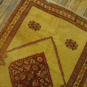 A gold and red patterned rug with detailed borders sits atop worn, distressed wide-plank wood floor.