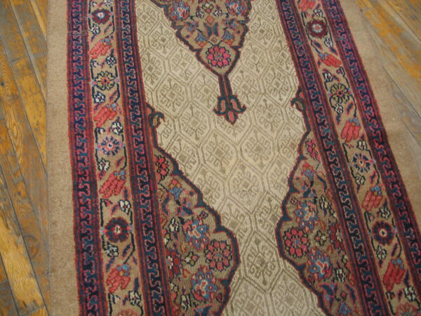 Traditional runner rug in beige, red, and dark blue with complex borders resting on wood flooring.