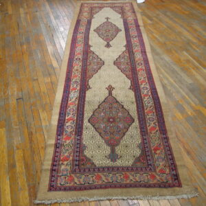 A beige and multi-colored runner rug with central medallions lies on worn, wide plank wooden floorboards.