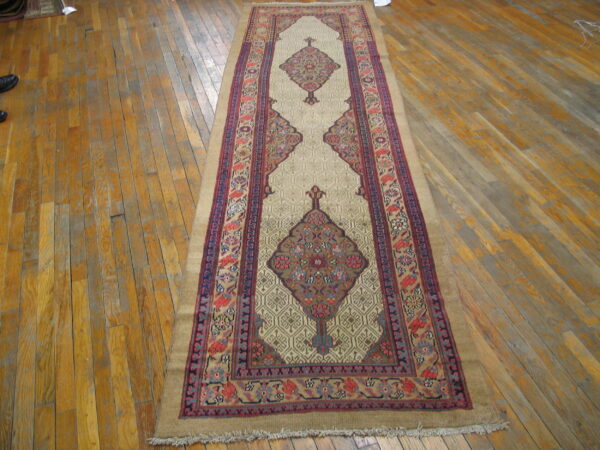A beige and multi-colored runner rug with central medallions lies on worn, wide plank wooden floorboards.