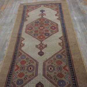 Geometric tan runner rug featuring red and blue medallion motifs on a textured beige field over rustic gray wood.