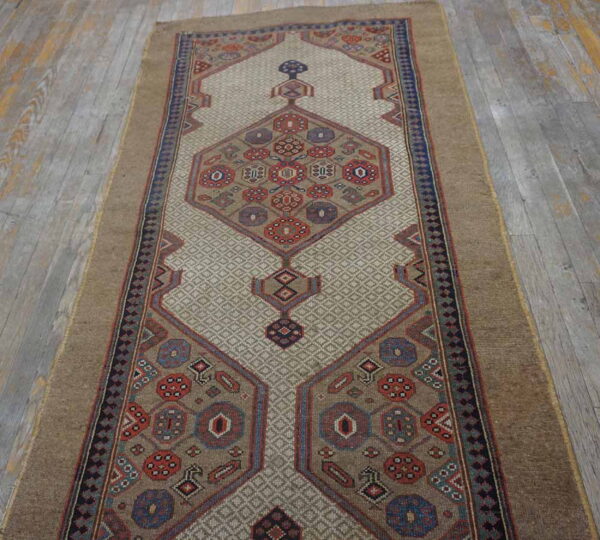 Geometric tan runner rug featuring red and blue medallion motifs on a textured beige field over rustic gray wood.