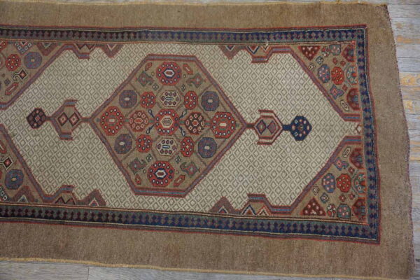 A brown runner rug featuring a beige diamond lattice field and colorful central geometric motifs rests on wood planks.