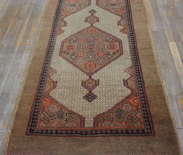 Brown and beige runner rug with geometric designs and colorful floral motifs on faded grey hardwood.