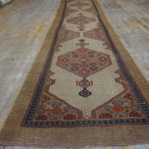 Geometric runner rug with a light beige field and brown border lying on distressed gray wood flooring.
